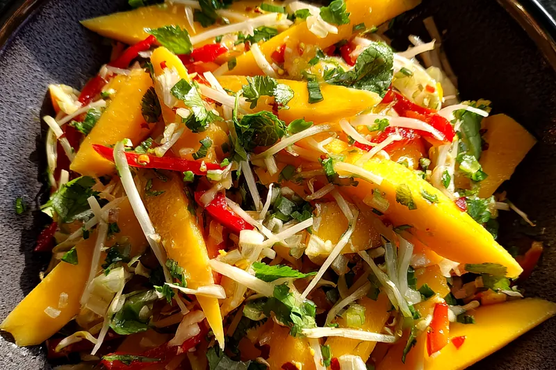 A hands-on image of preparing Vibrant Thai Mango Salad, showing fresh ingredients being mixed together.